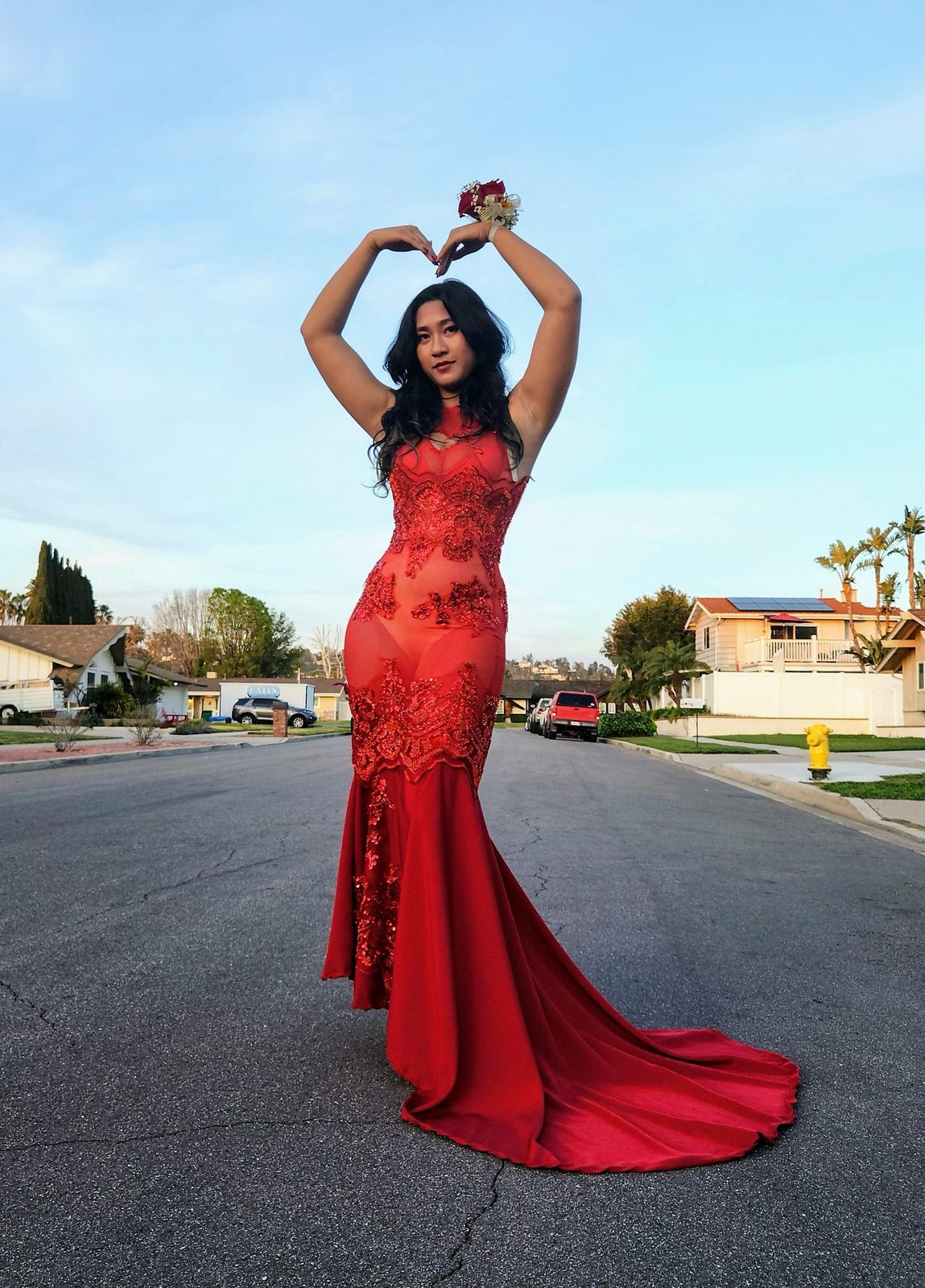 Model in a red lace mermaid gown with a sweep train, arms raised in a heart shape